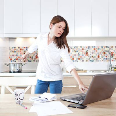 Beautiful young woman working on laptop and cooking at the same time