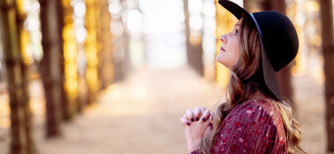 Selective focus shot of a beautiful young lady praying in a forest