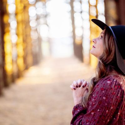 Selective focus shot of a beautiful young lady praying in a forest
