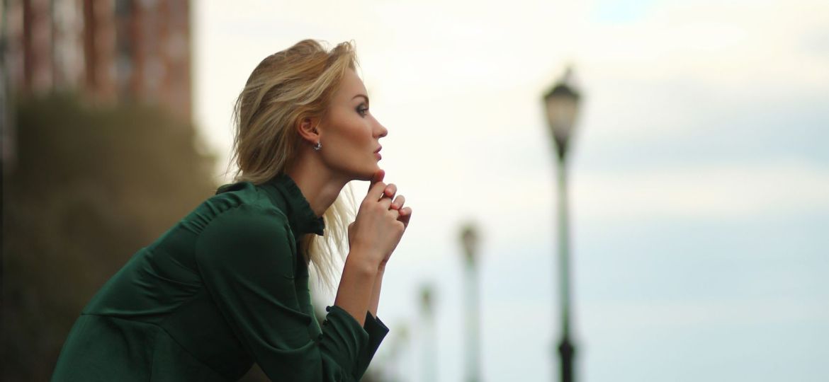 Thoughtful woman in green dress sits on the bench