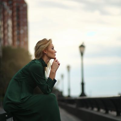 Thoughtful woman in green dress sits on the bench