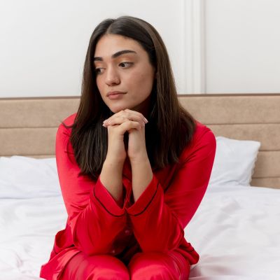 young-beautiful-woman-red-pajamas-sitting-bed-looking-aside-with-sad-expression-face-bedroom-interior-light-background