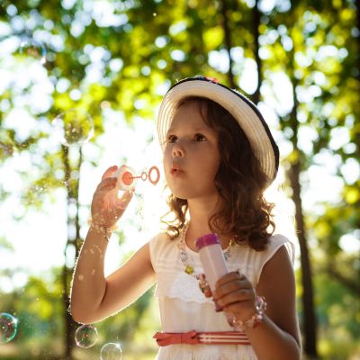 Young pretty girl blowing bubbles, walking in park at sunset.